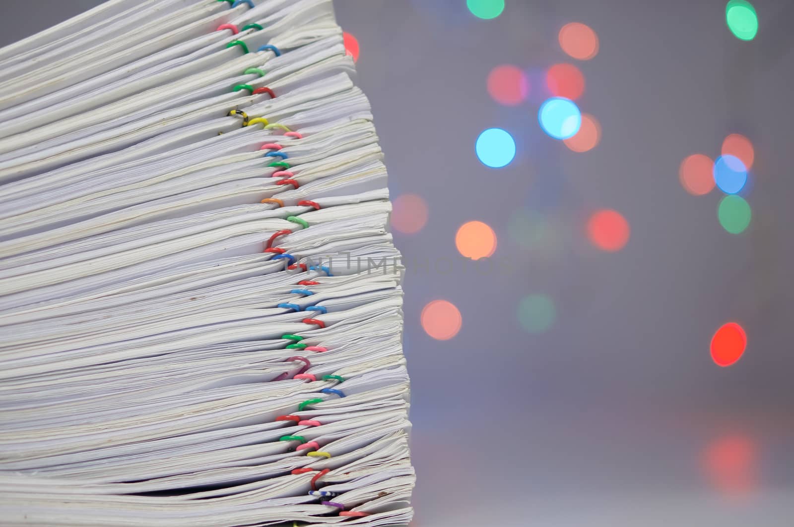 Stack of paperwork with colorful paperclip have colorful bokeh circle or defocused of glitter as background.