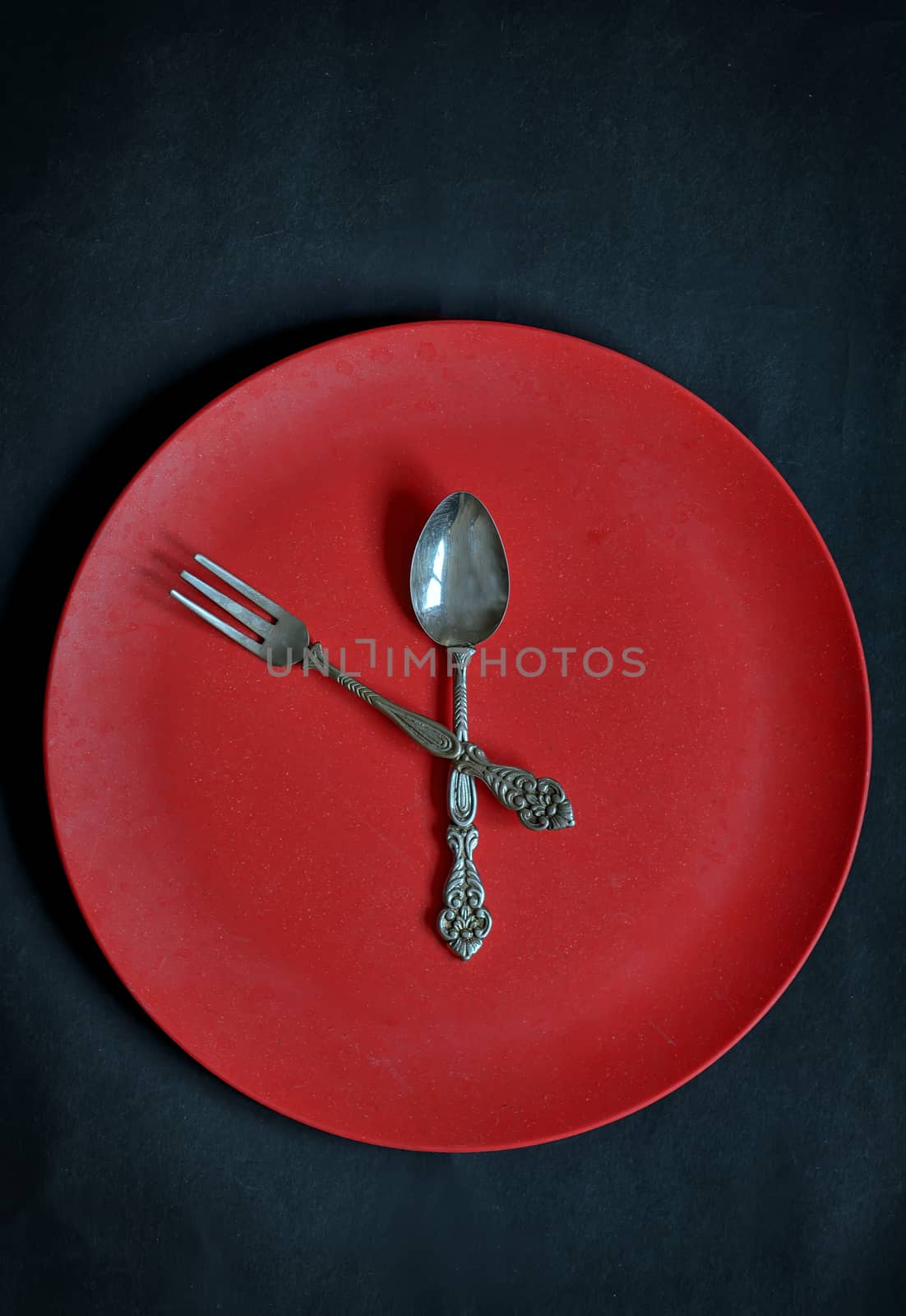 Clock with red plate, spoon and fork  on rusty background