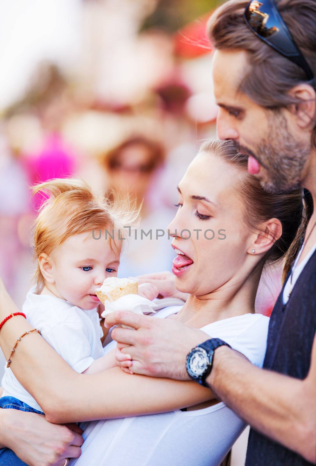 Mother and a father are hugging a baby boy and feeding him with ice cream outdoors. Copy space.