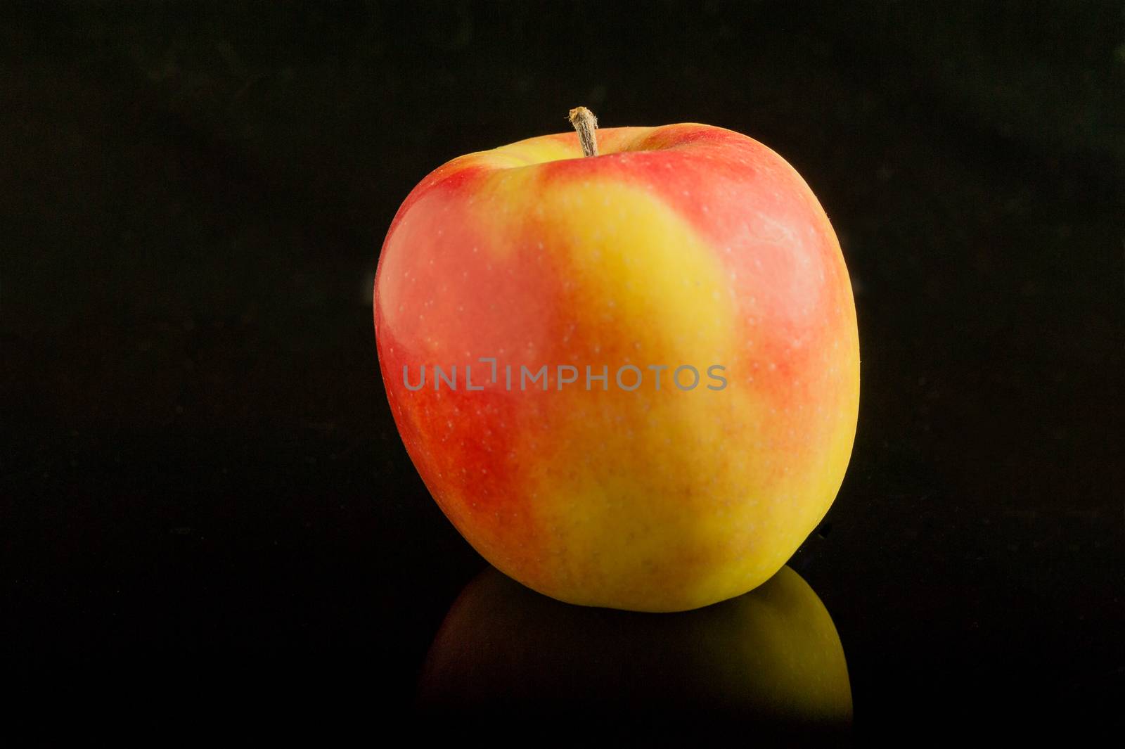 Beautiful yellow-red apple  lie on a black glass table with reflection