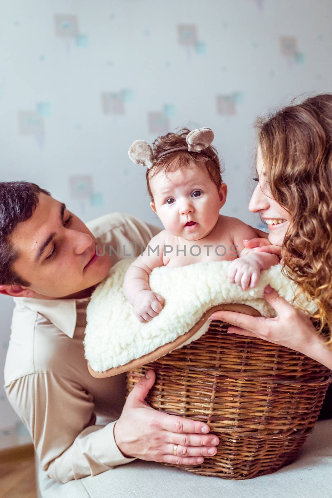 naked baby with her parents sitting in the wicker basket on the white soft blanket