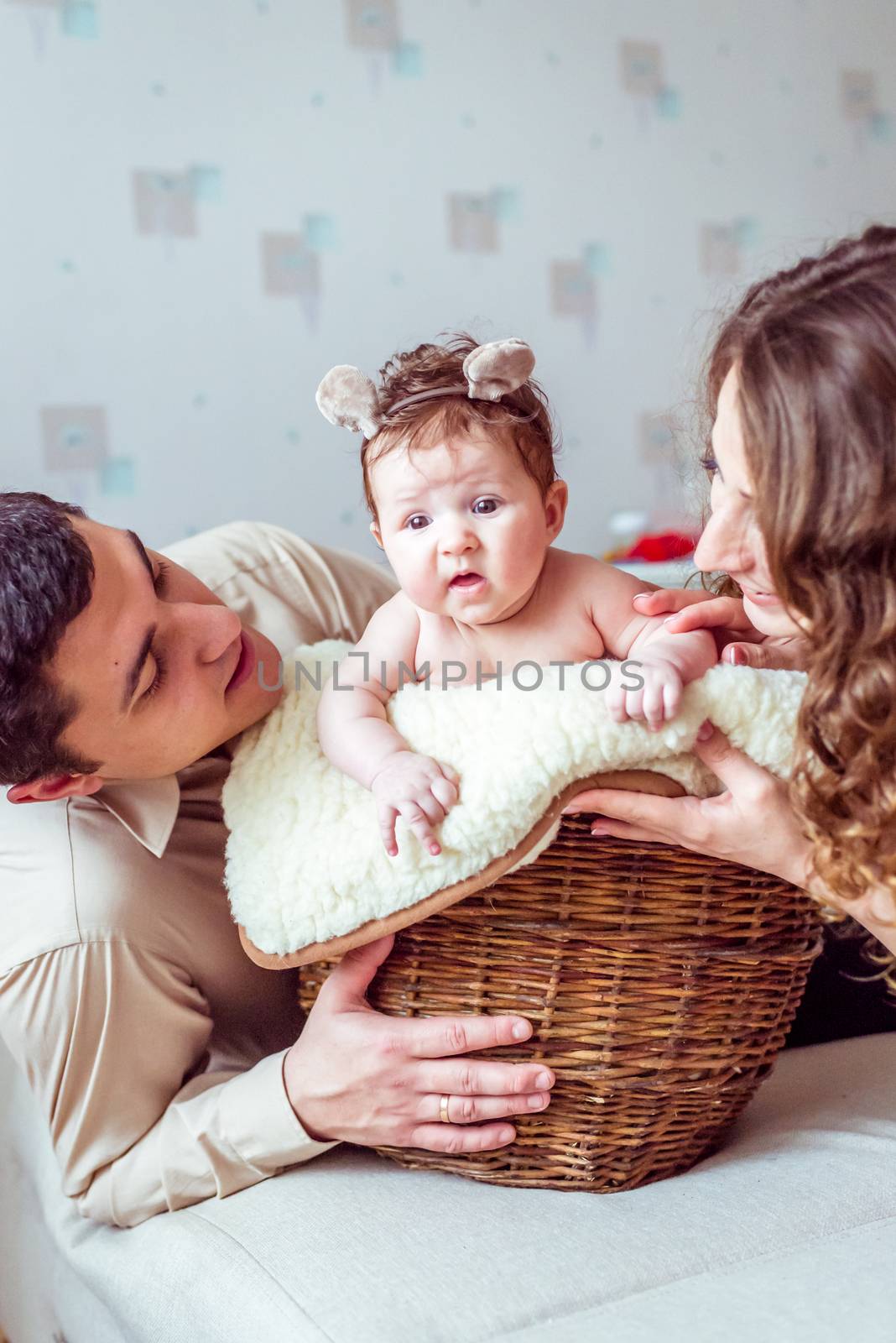 naked baby with her parents sitting in the wicker basket on the white soft blanket