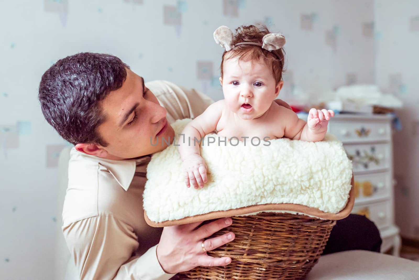 naked baby with her father sitting in the wicker basket on the white soft blanket