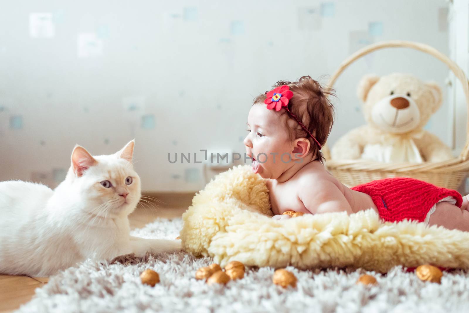 naked baby lying on soft blanket and watching a cat