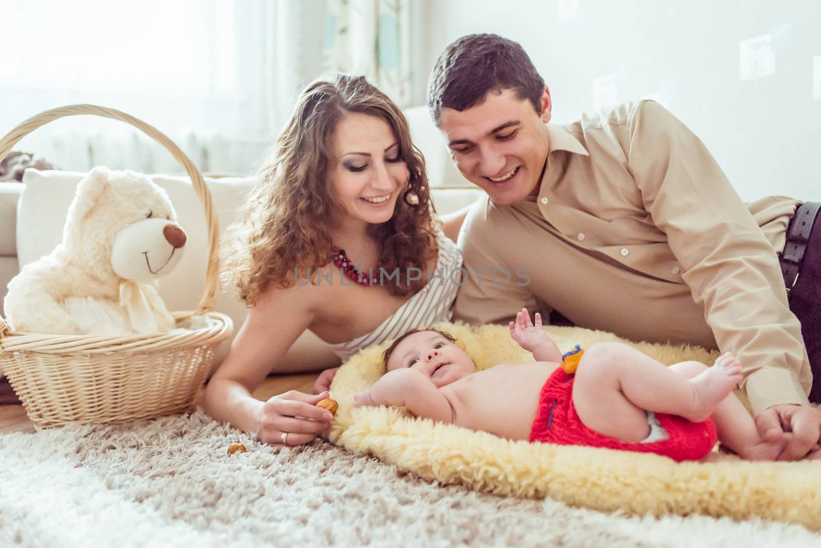 naked baby with her parents lying on soft blanket in the room