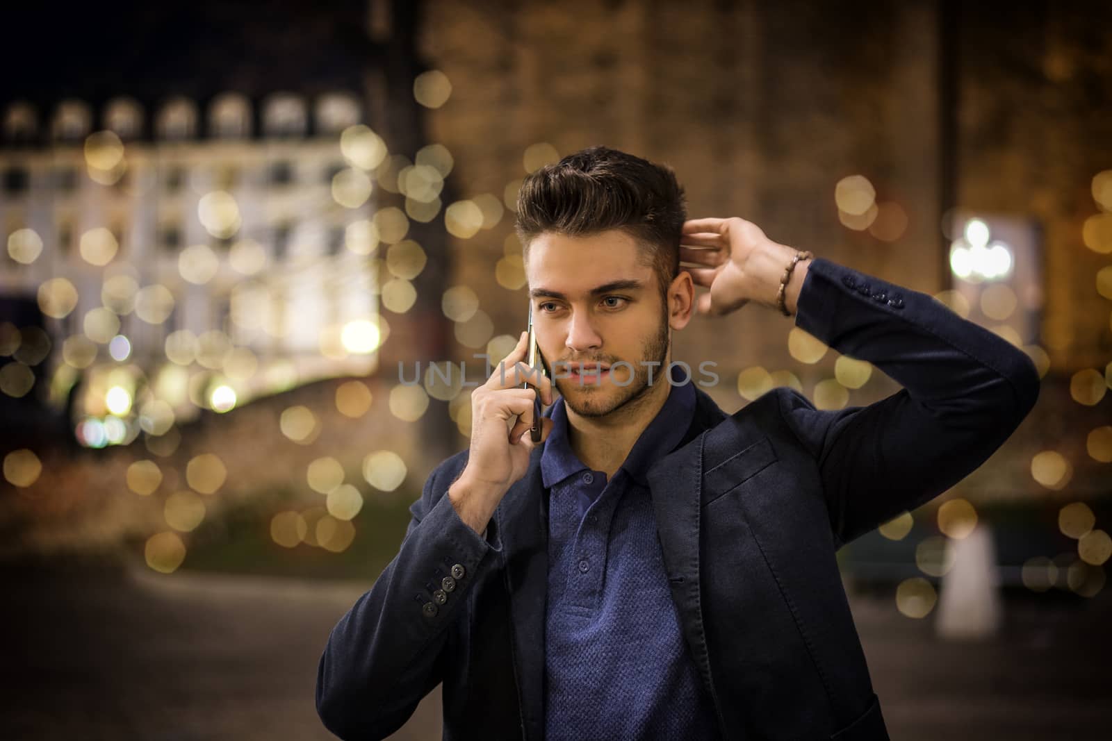 Attractive young man portrait at night talking on the phone, with city lights behind him in Turin, Italy