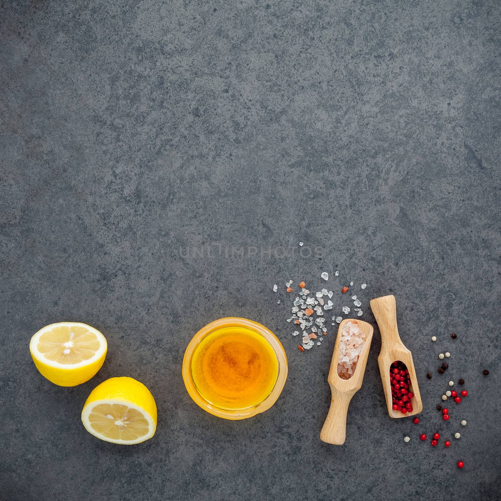 The lemon vinaigrette dressing ingredients lemon, olive oil, himalayan salt and pepper corn on dark stone background with flat lay and copy space.