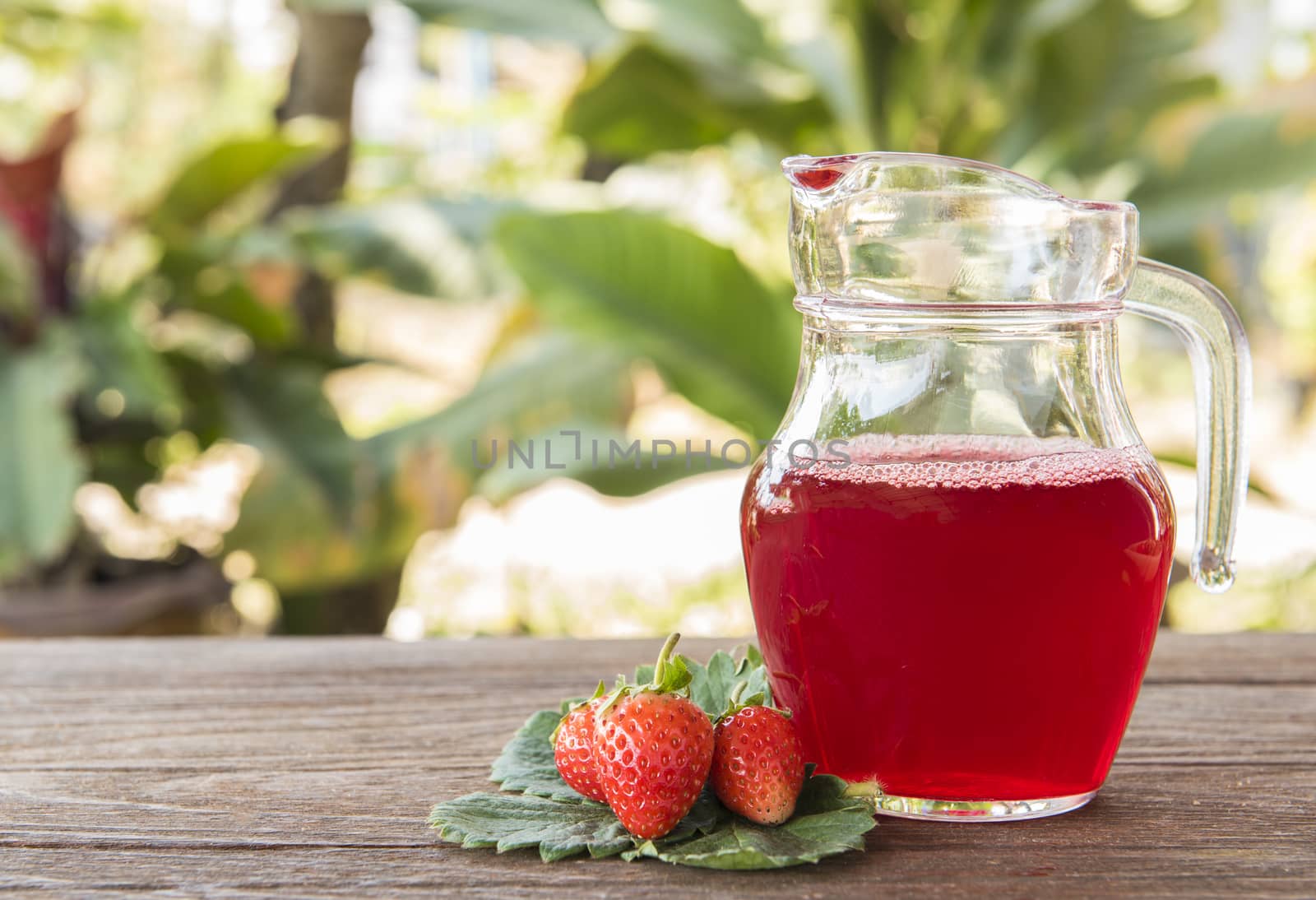 Fresh strawberry juice in a jug is placed on a wooden table.