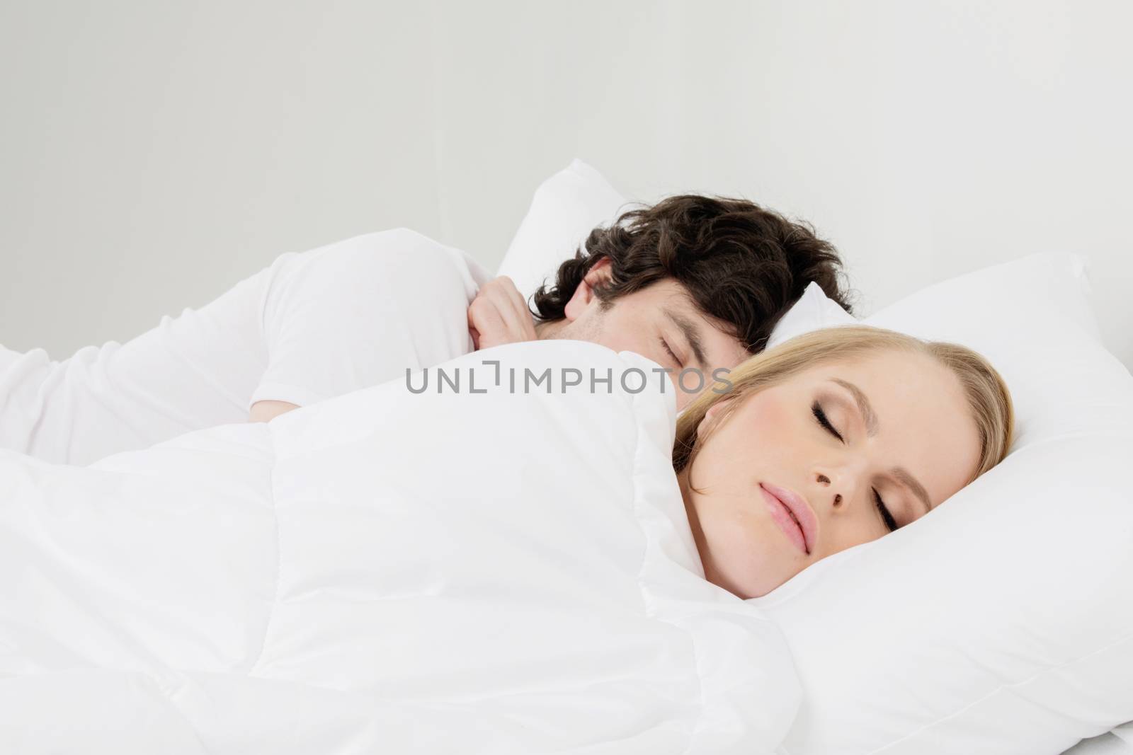 Young couple sleeping in bed with white blanket and pillows