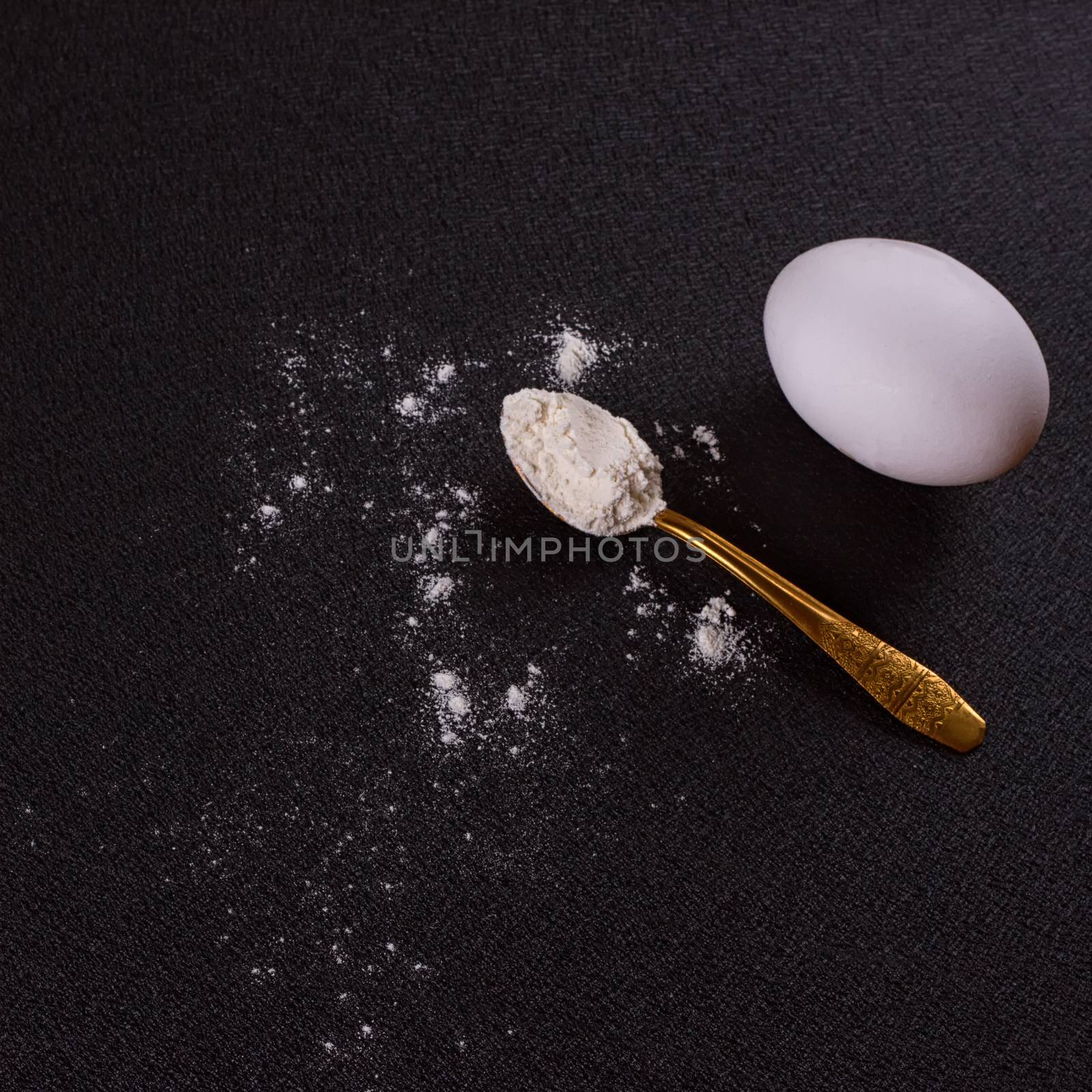 Gold-plated spoon, flour, egg on a black background