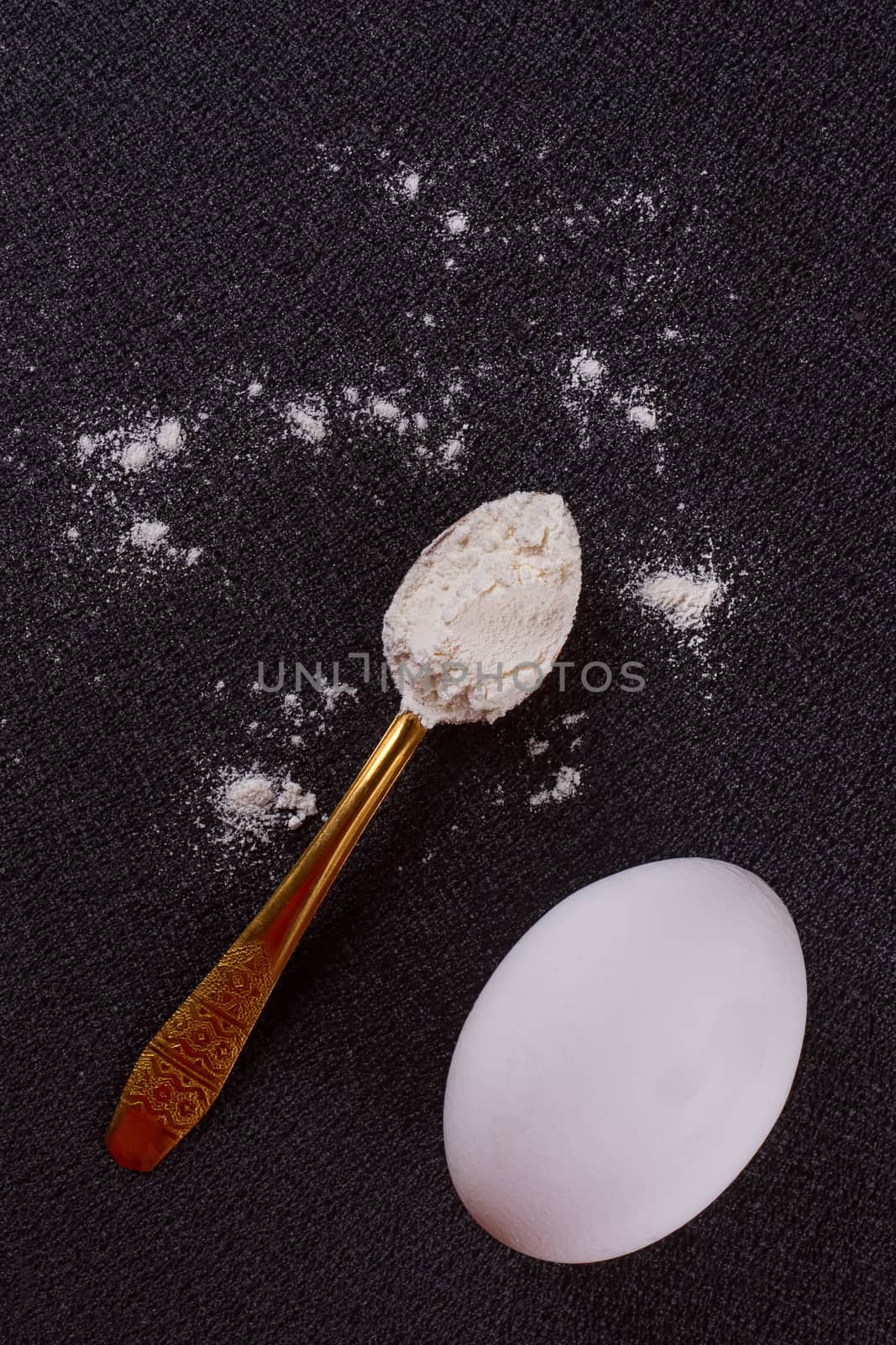 Gold-plated spoon, flour, egg on a black background