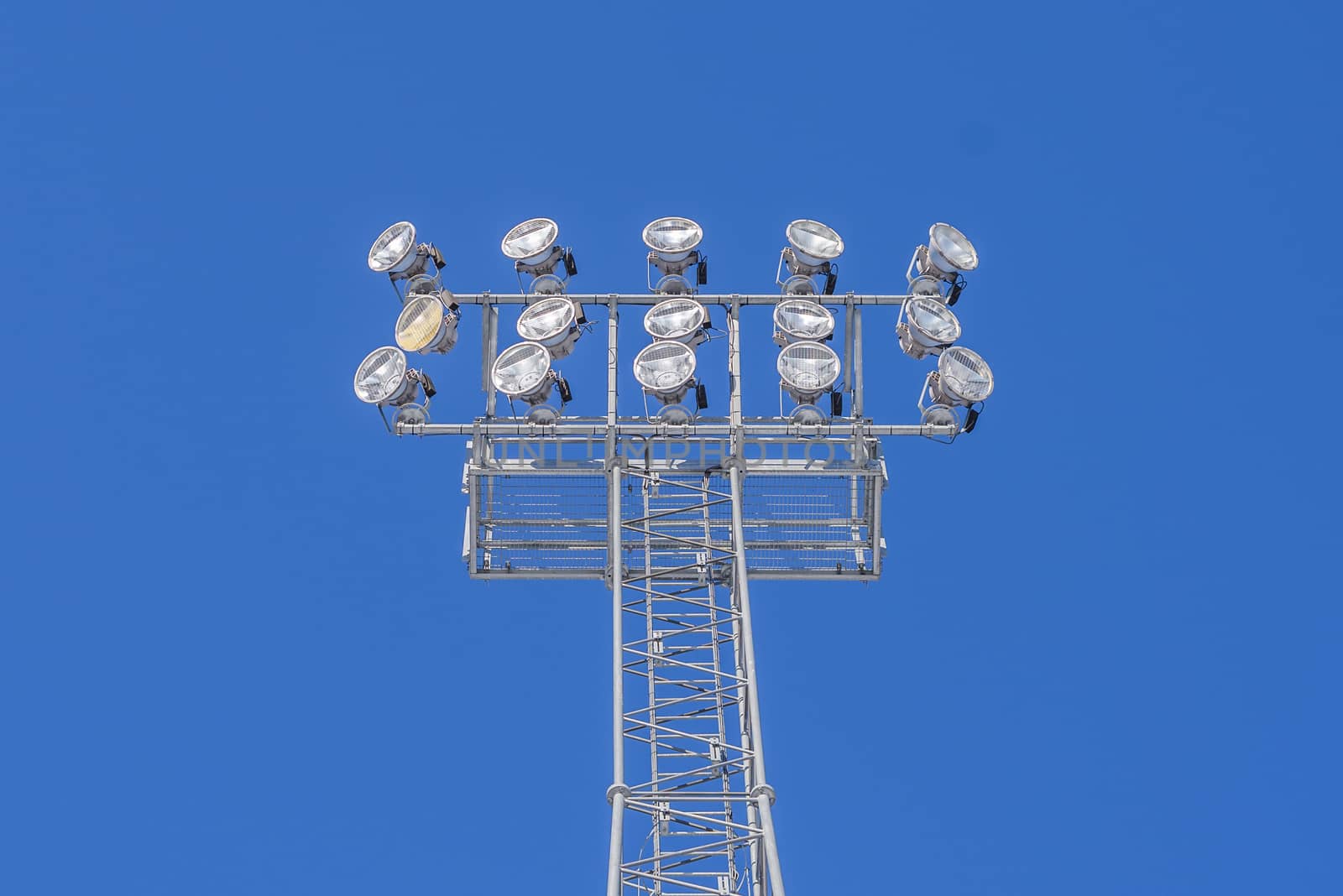 Stadium lights switched off on a metallic tower against a blue sky.