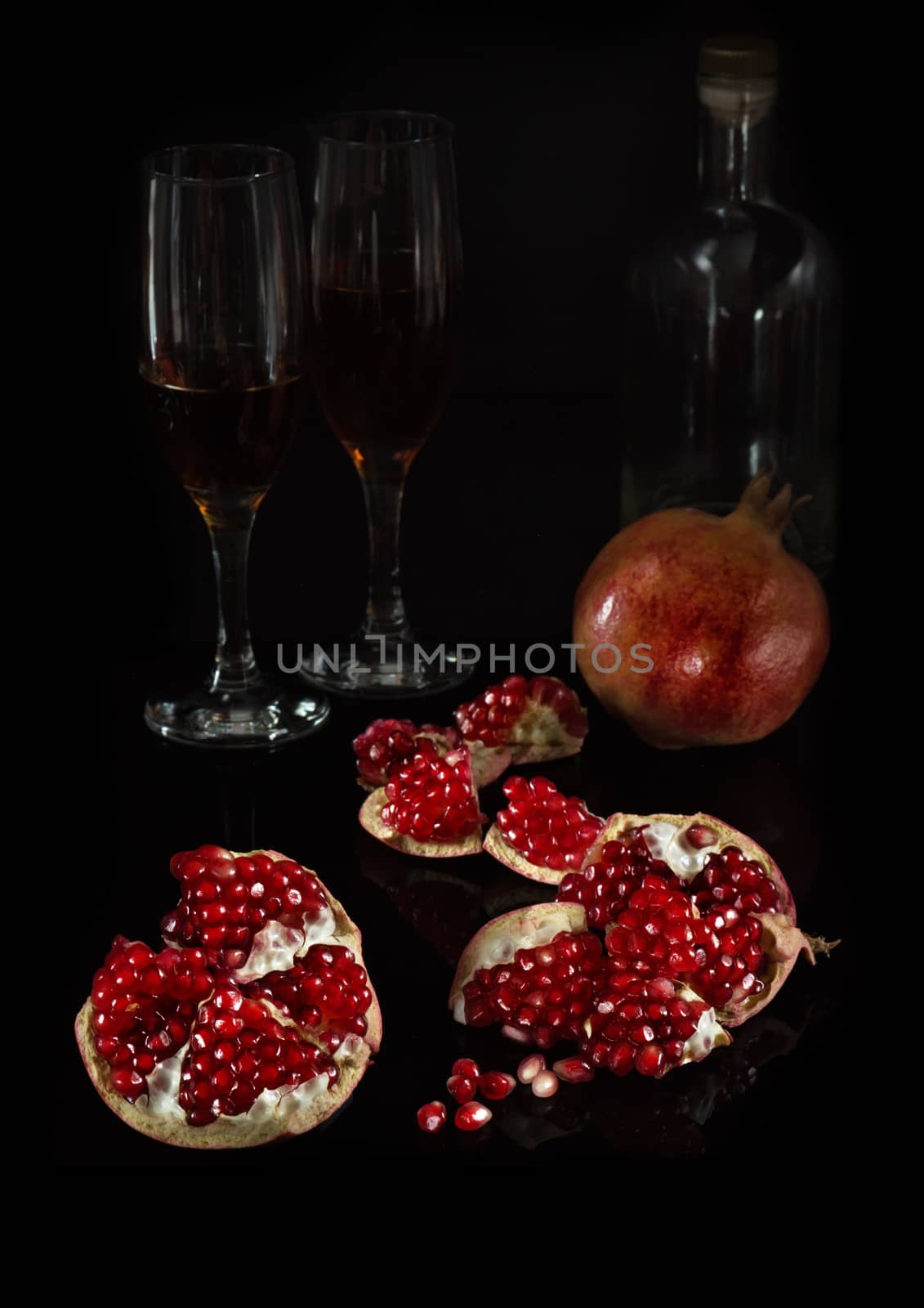 Segments of pomegranate and the whole fruit on a black background with glasses