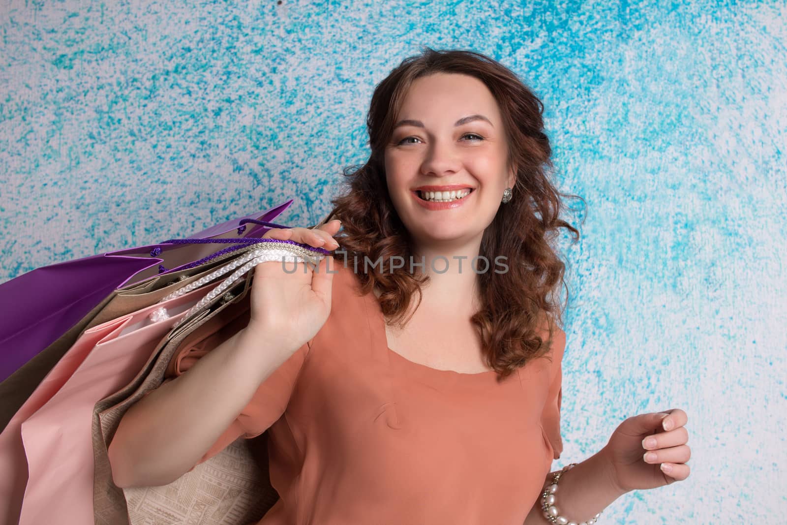 Happy smiling woman at shopping holding colourful paper bags near blue wall