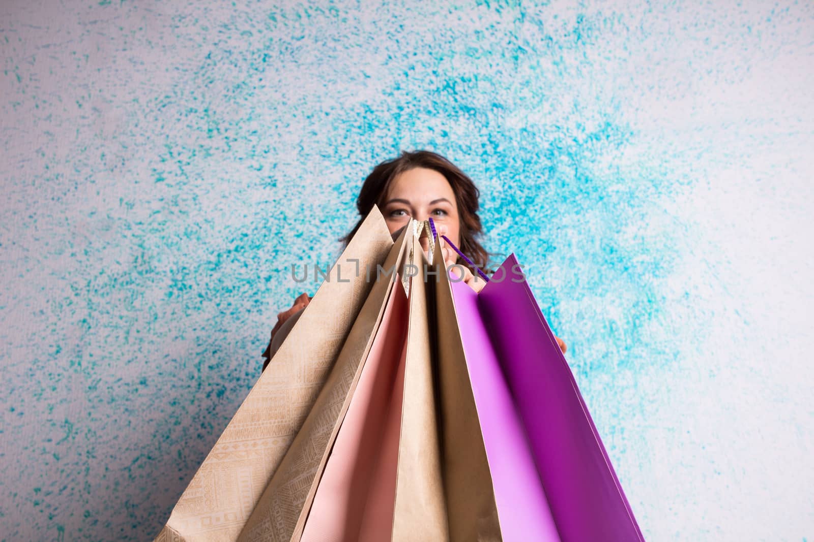 Happy smiling woman at shopping showing colourful paper bags near blue wall