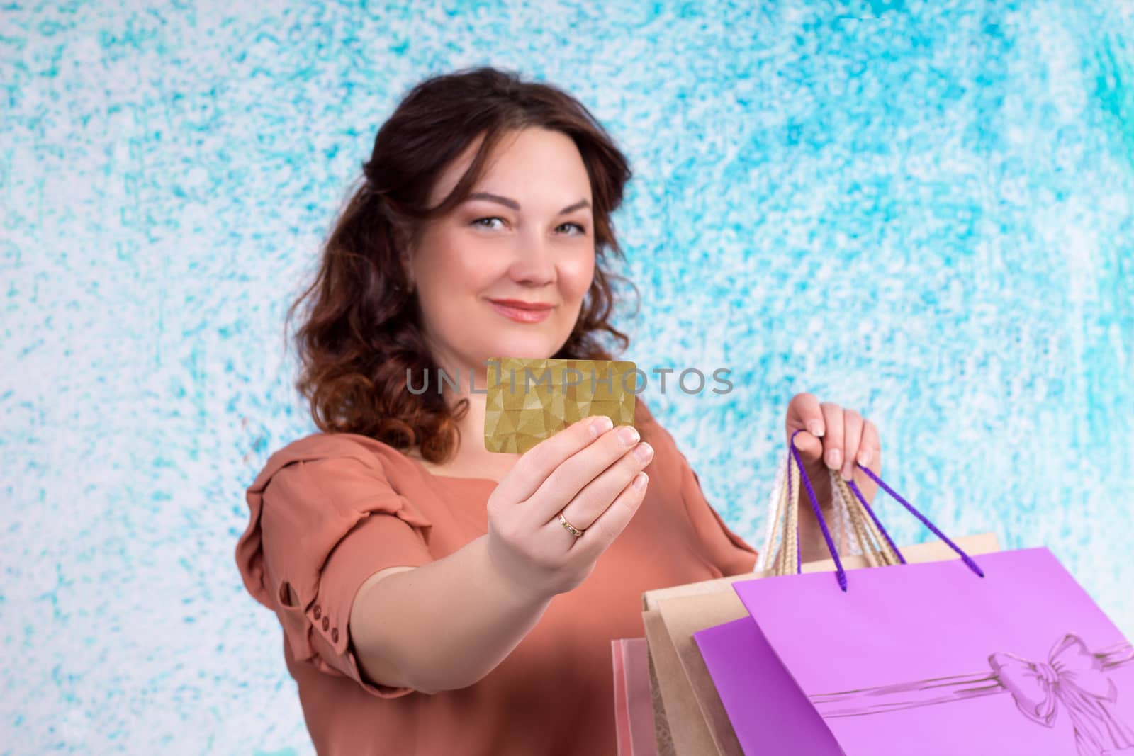 Happy smiling woman holding colourful shopping paper bags shows banking credit card