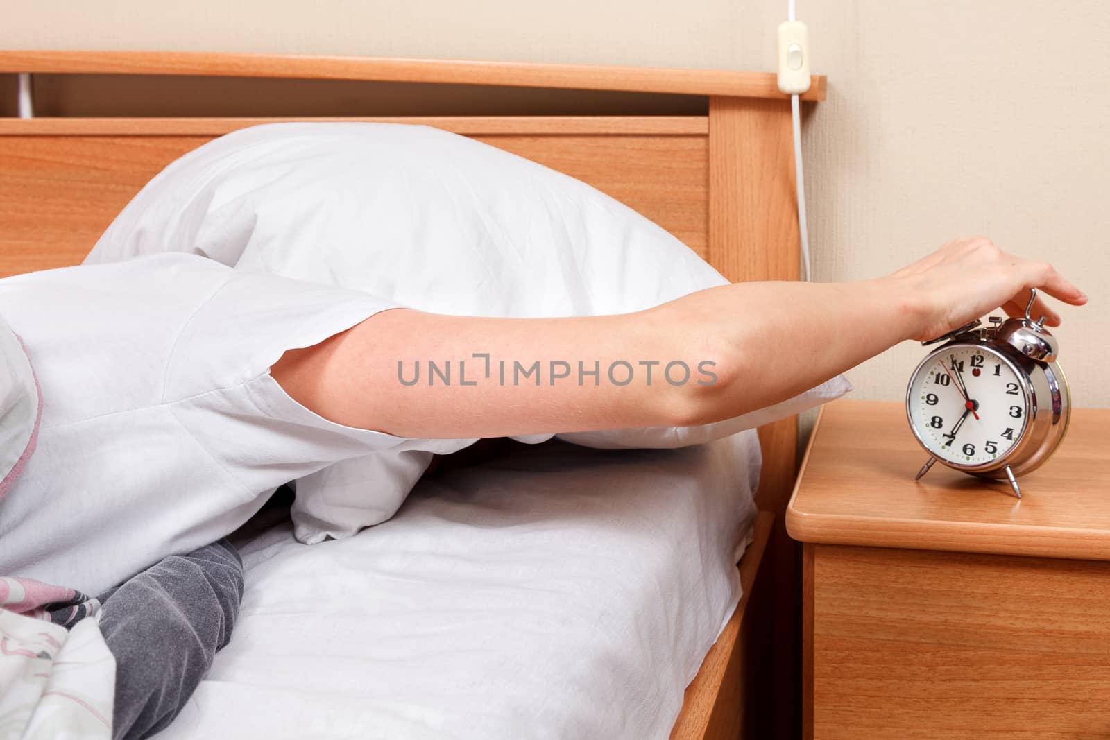 Woman turning off her alarm clock in her bedroom by Nobilior