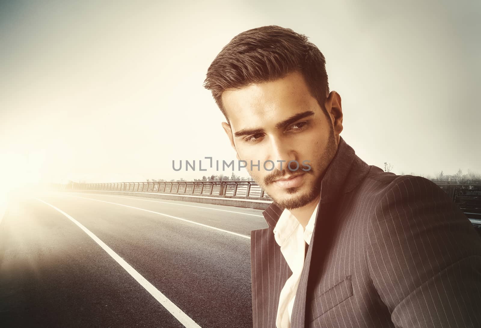 Confident stylish man standing on a roadside and looking away. Horizontal outdoors shot.