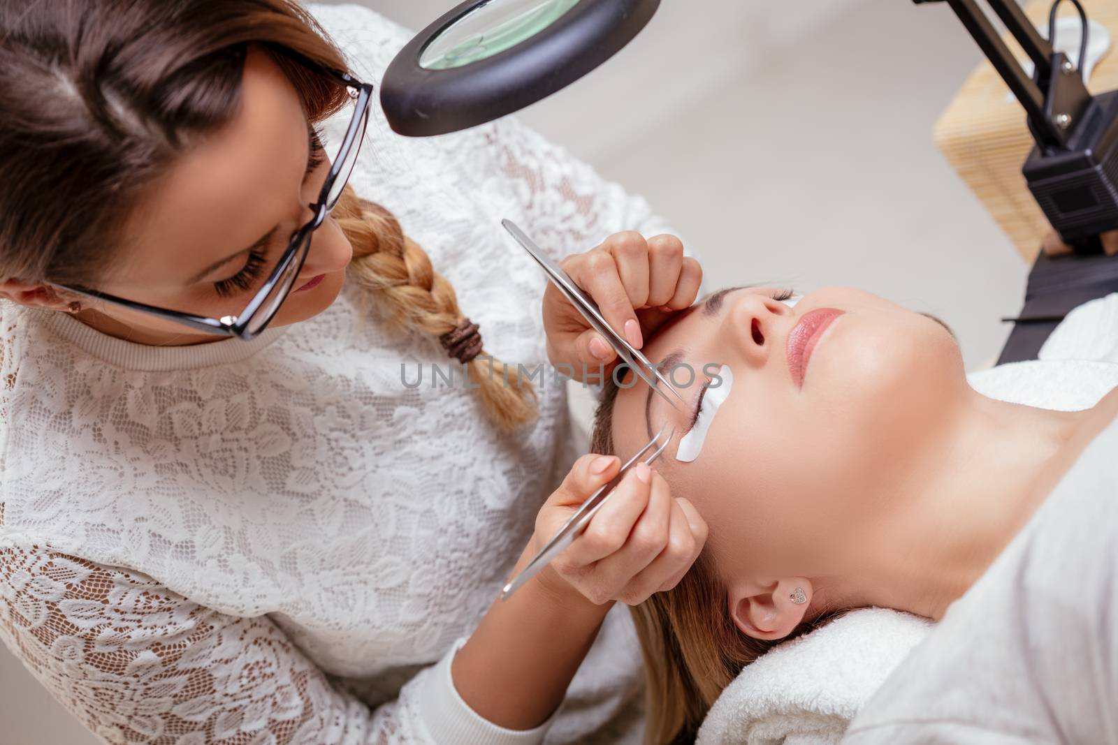 Beautician applying extended eyelashes to model at the beauty salon.