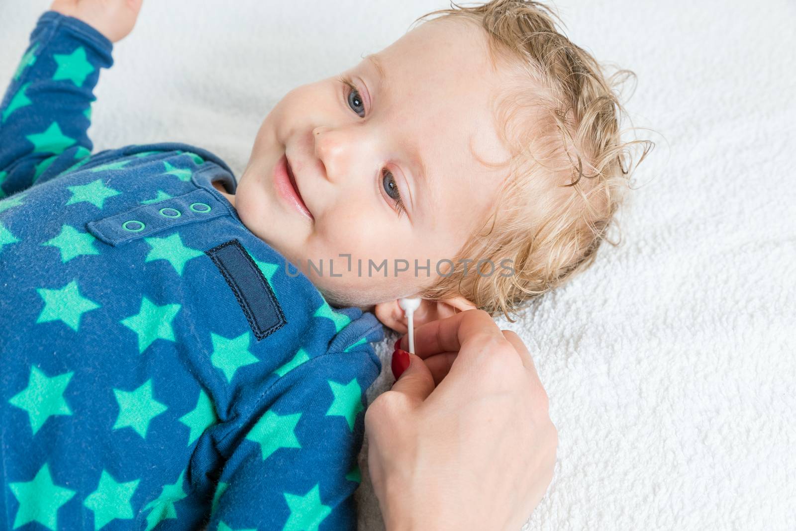 Mother hand cleaning baby ear with cotton swab,infant lying with wet hair and blue eyes and smiling,copy space,horizontal photo.