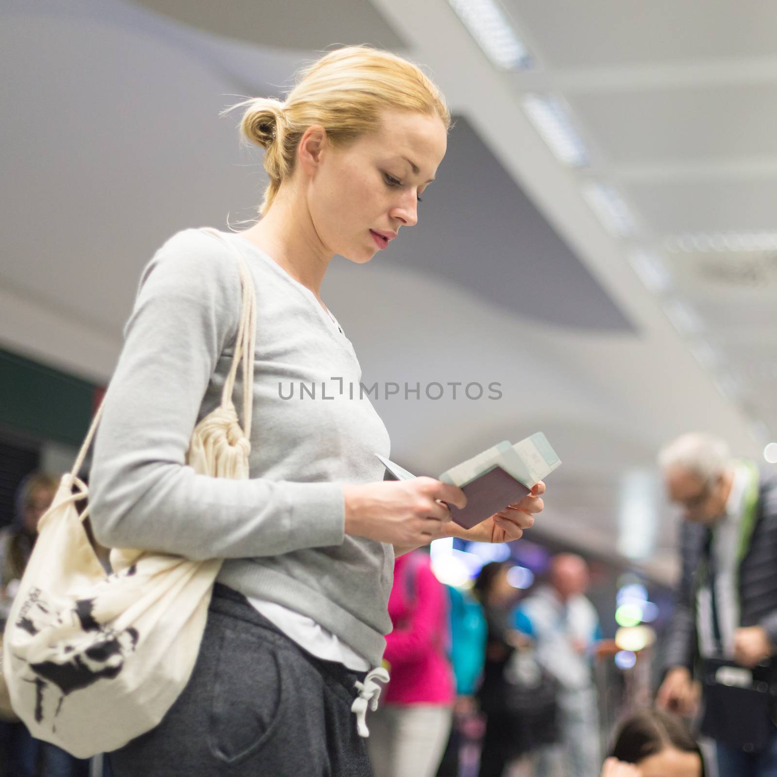 Casualy dressed woman checking flight informations on airplane ticket while waiting for her flight at airport.