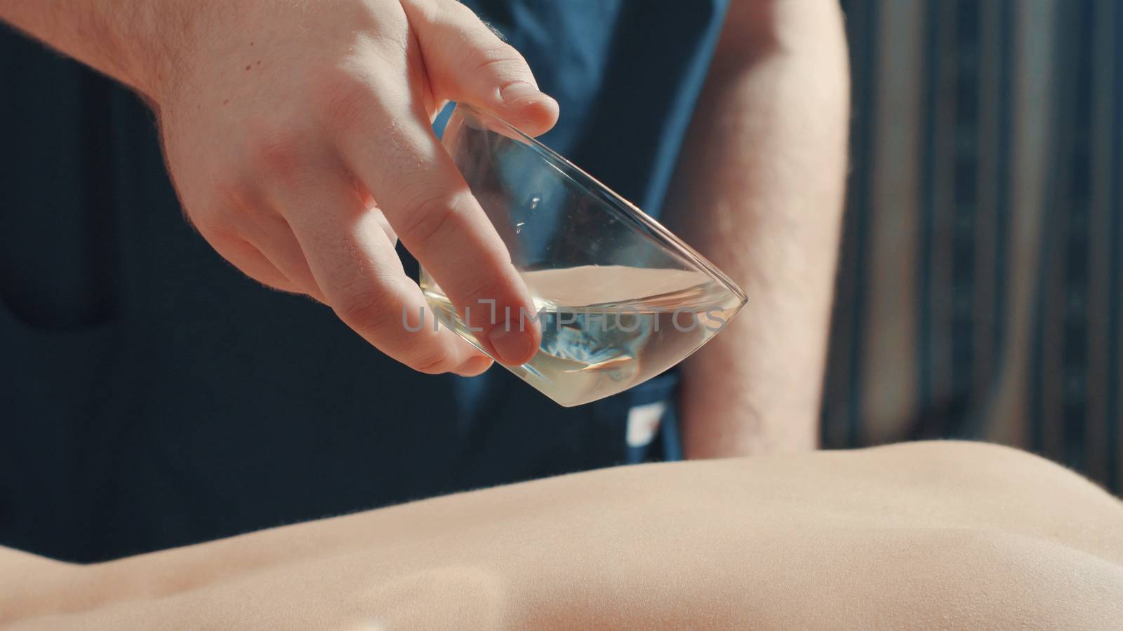 Massagist's hand pouring oil on the woman's back, close up