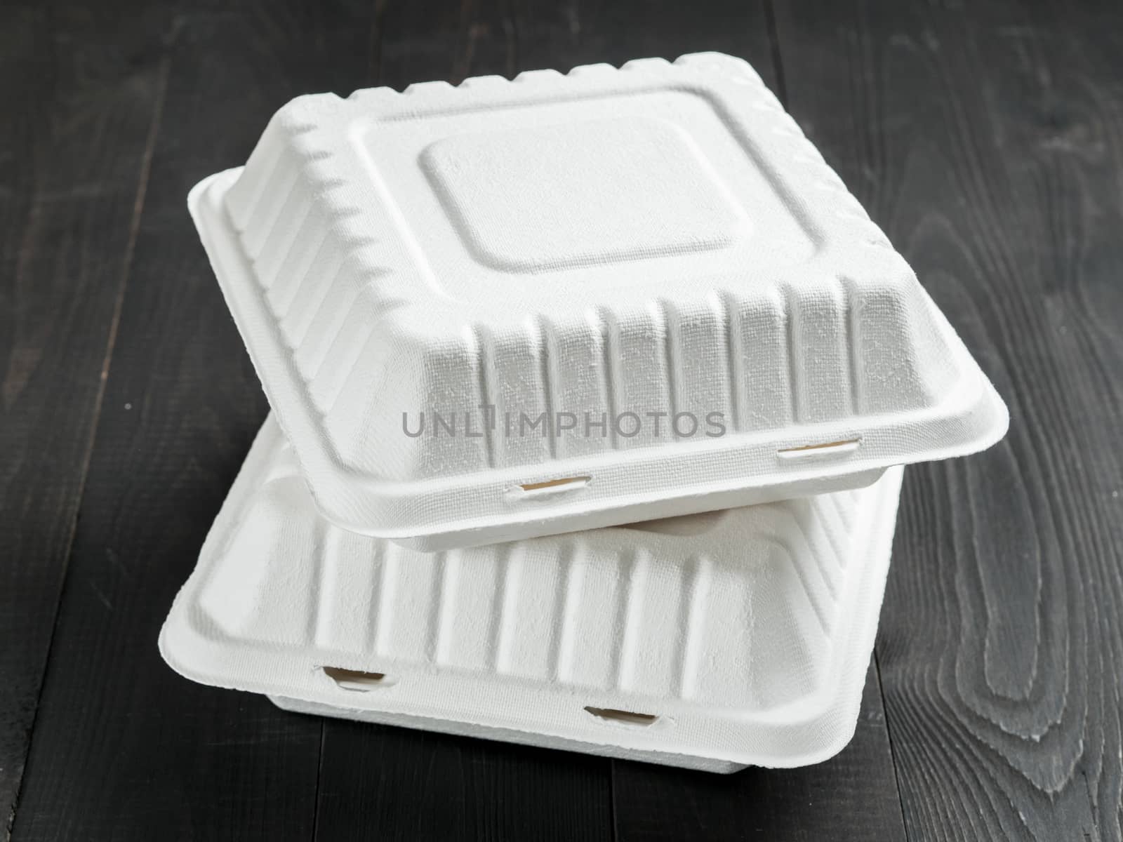 Two closed disposable take out container. Gray closed cardboard lunch box on dark wooden background
