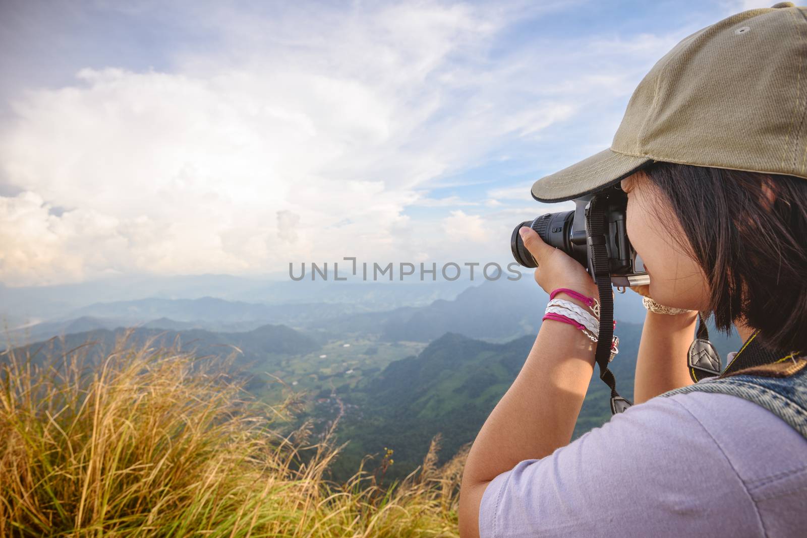 Side face of hiker teens girl wear caps with digital camera taking photo beautiful landscape natural of sierra and sky on mountain at viewpoint Phu Chi Fa Forest Park, Chiang Rai, Thailand
