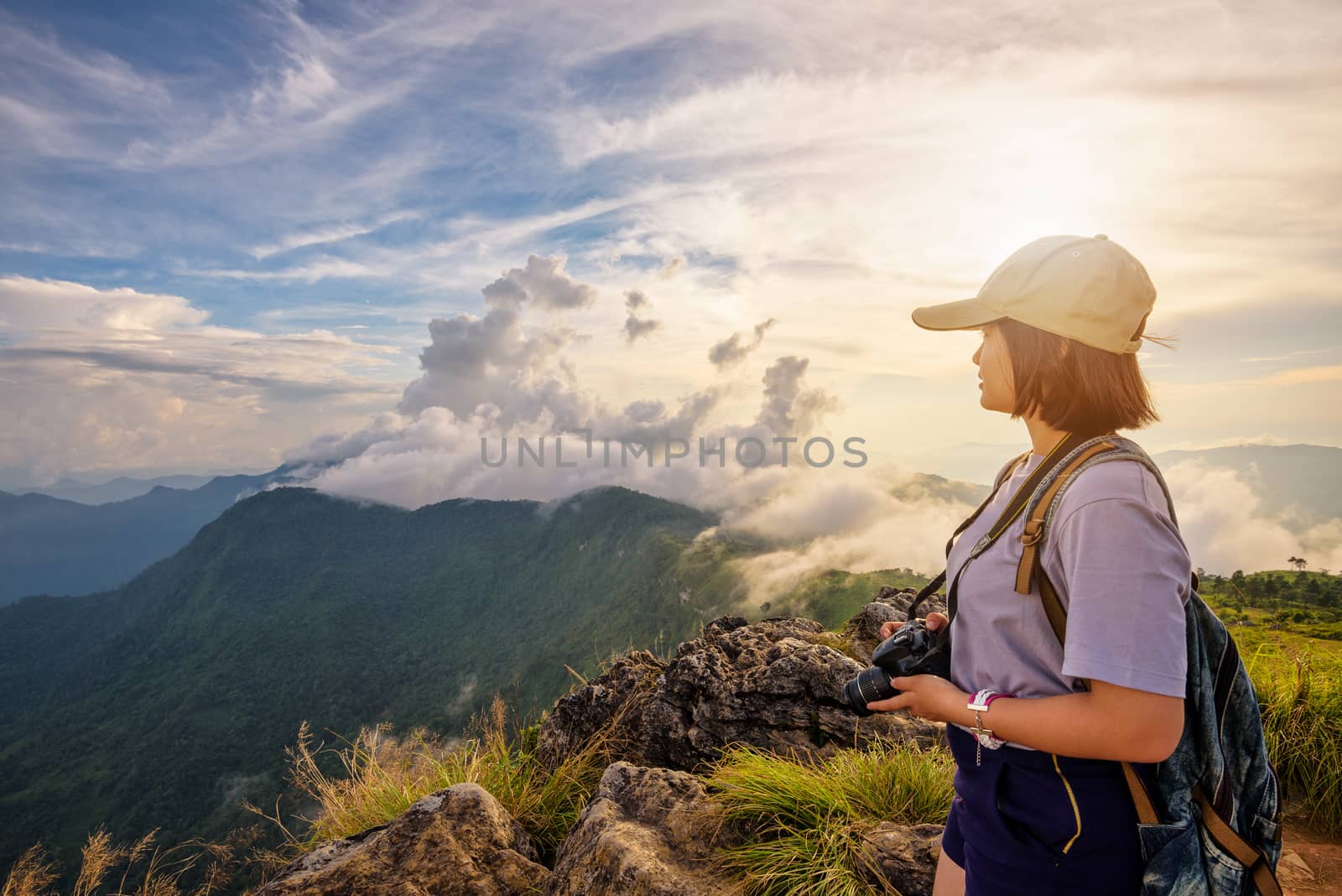 Hiker asian young woman happy with camera backpack and caps looking beautiful landscape nature of mountain and colourful sky at sunset on viewpoint Phu Chi Fa Forest Park, Chiang Rai, Thailand