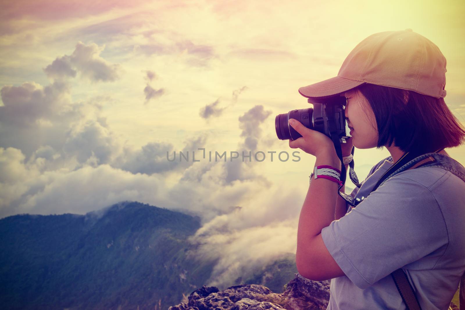 Vintage style hiker asian teens girl with digital camera taking photo beautiful landscape natural of sierra and sky during sunset on mountain at Phu Chi Fa Forest Park, Chiang Rai, Thailand