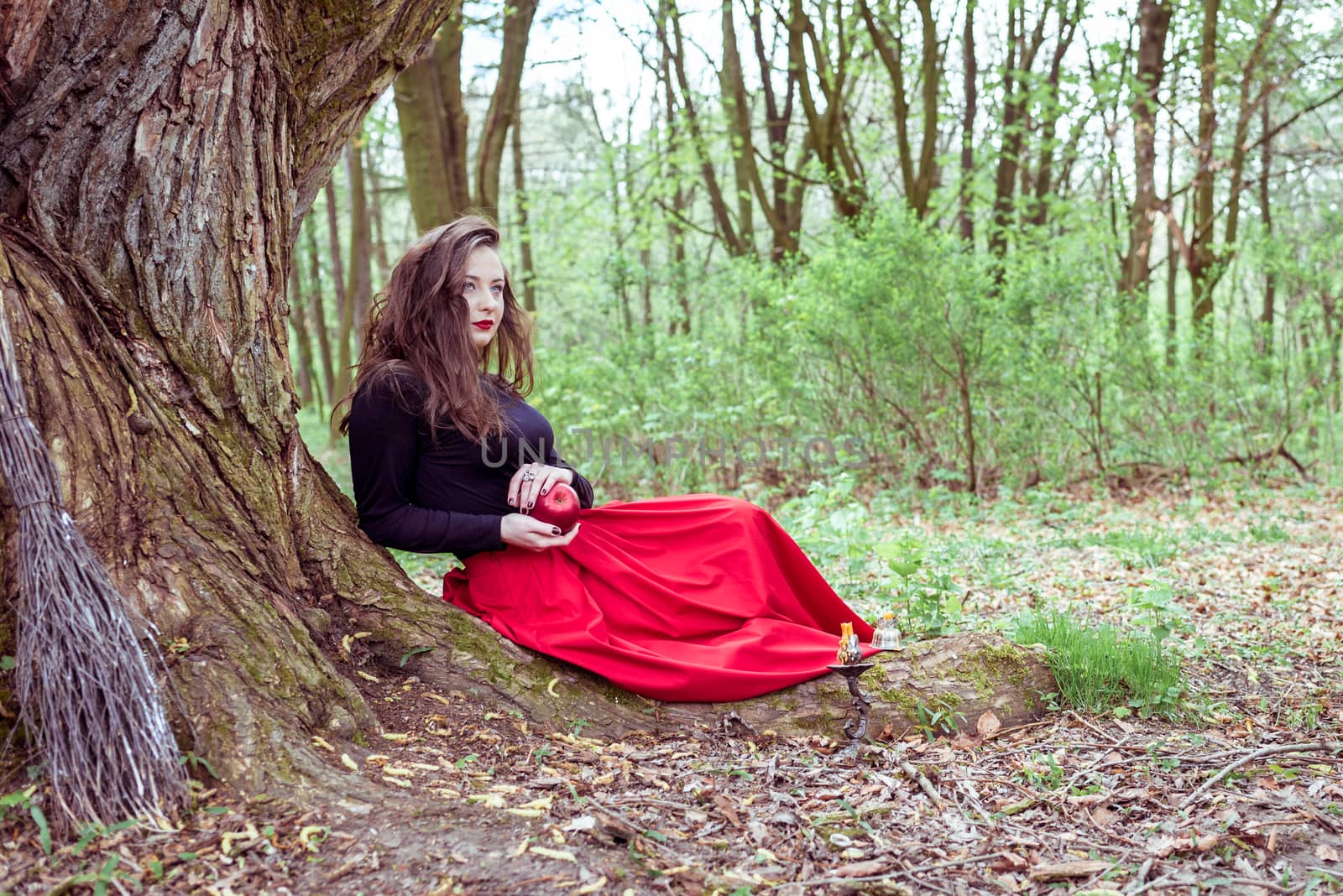 mystical witch woman sitting under a old tree in the forest