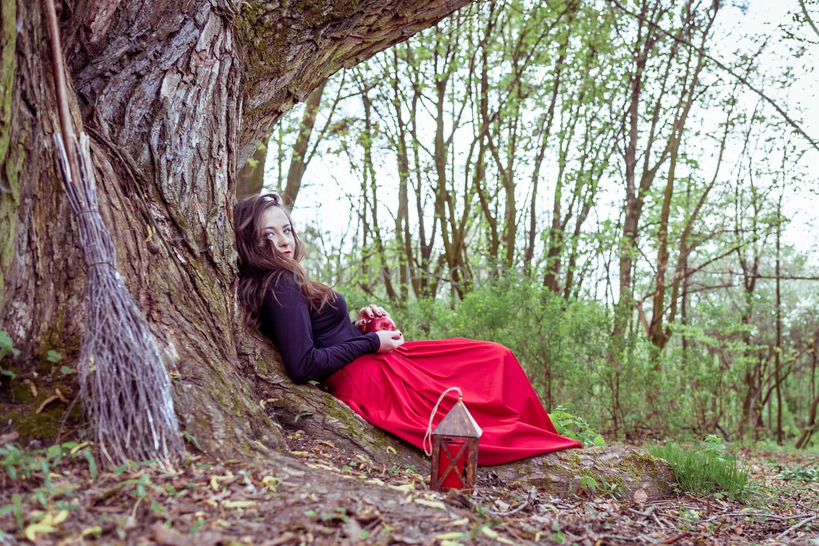 mystical witch woman sitting under a old tree in the summer park