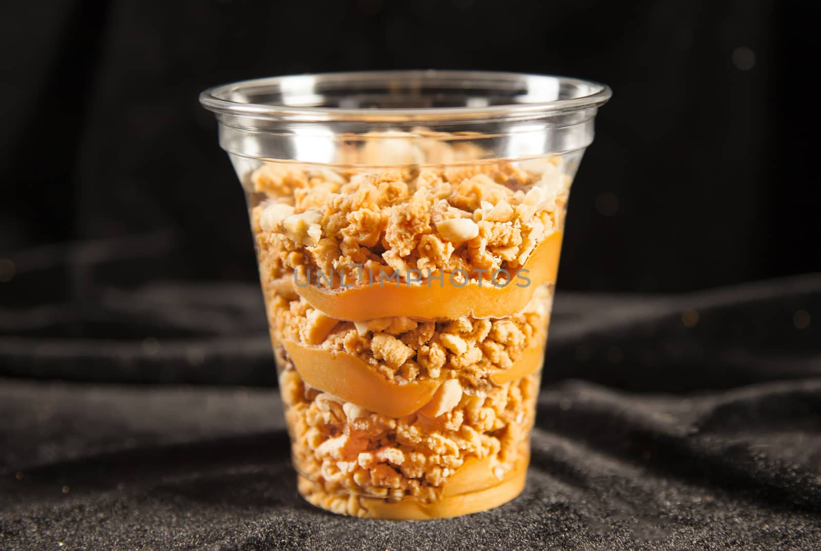 Sweet peanut cake in plastic cup on black background