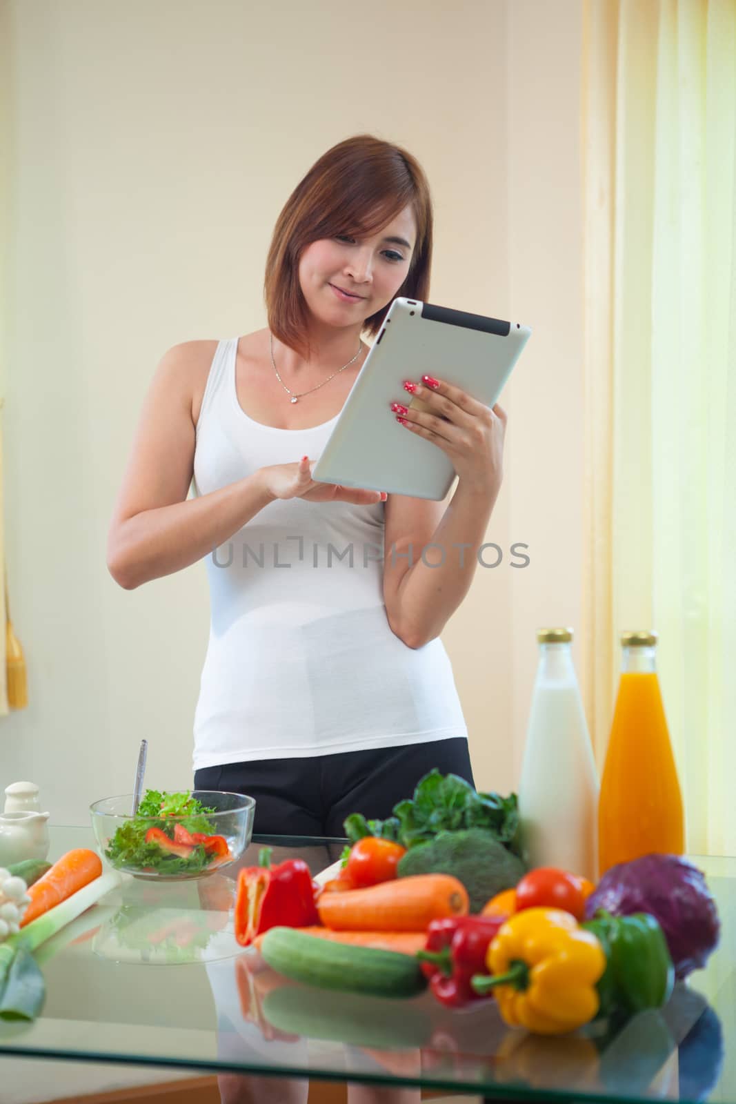 Young asian woman In Kitchen Following Recipe On Digital Tablet