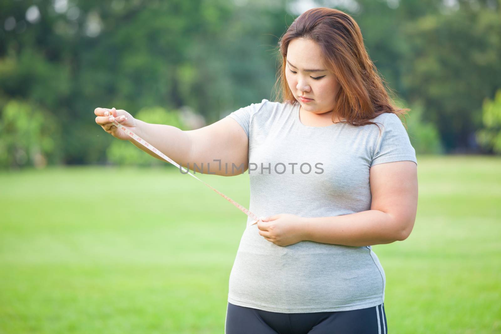 Happy fat asian woman measuring her stomach in the park