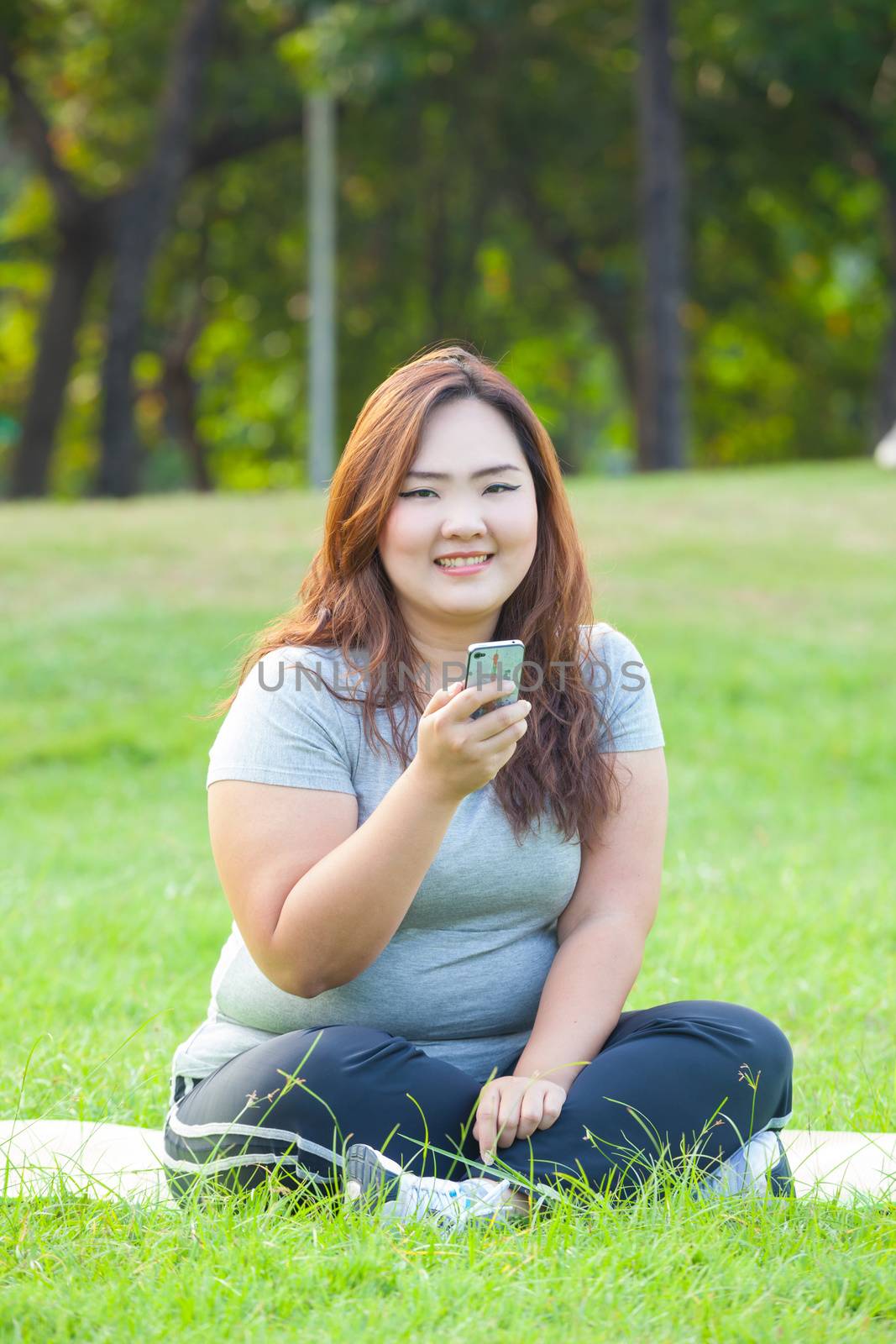 Happy fatty asian woman using mobile phone outdoor in a park