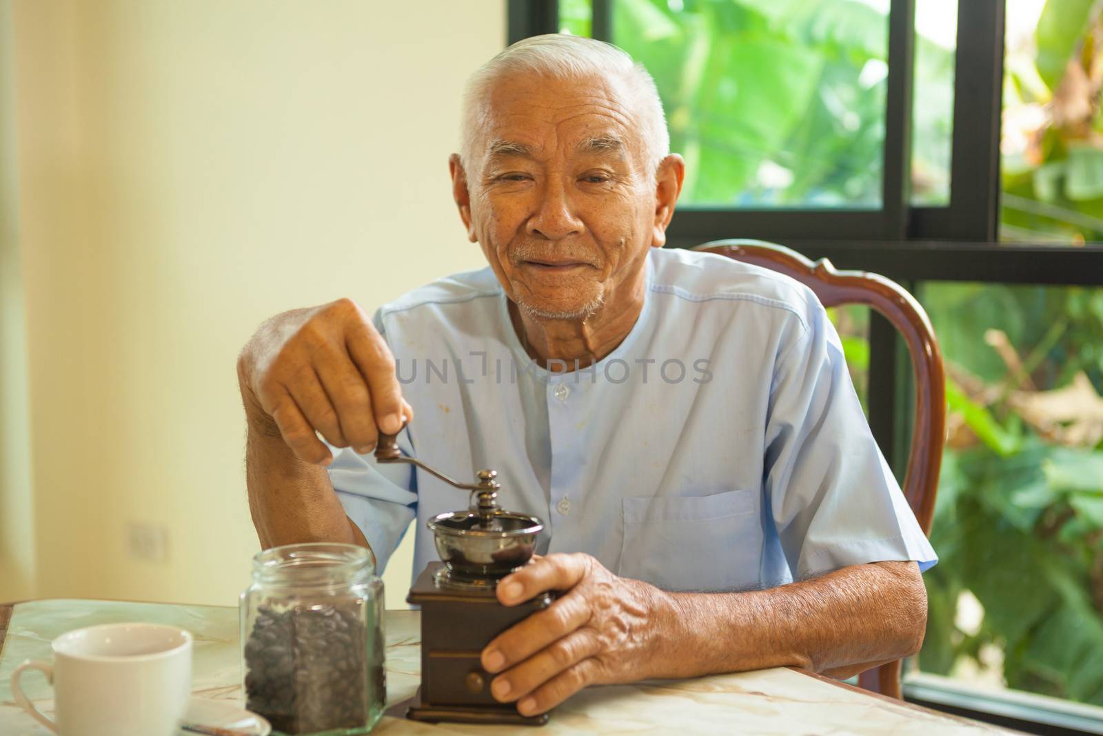 Asian senior man with vintage coffee grinder and coffee beans