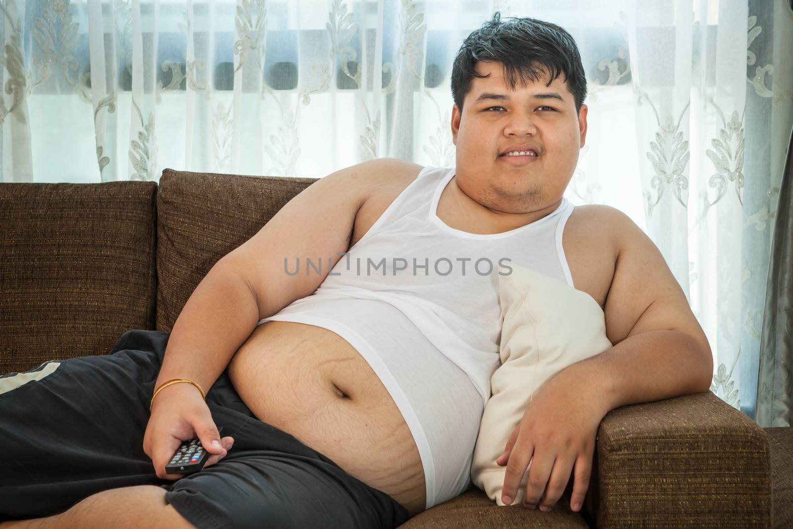 Overweight guy sitting on the couch to watch some TV by witthaya