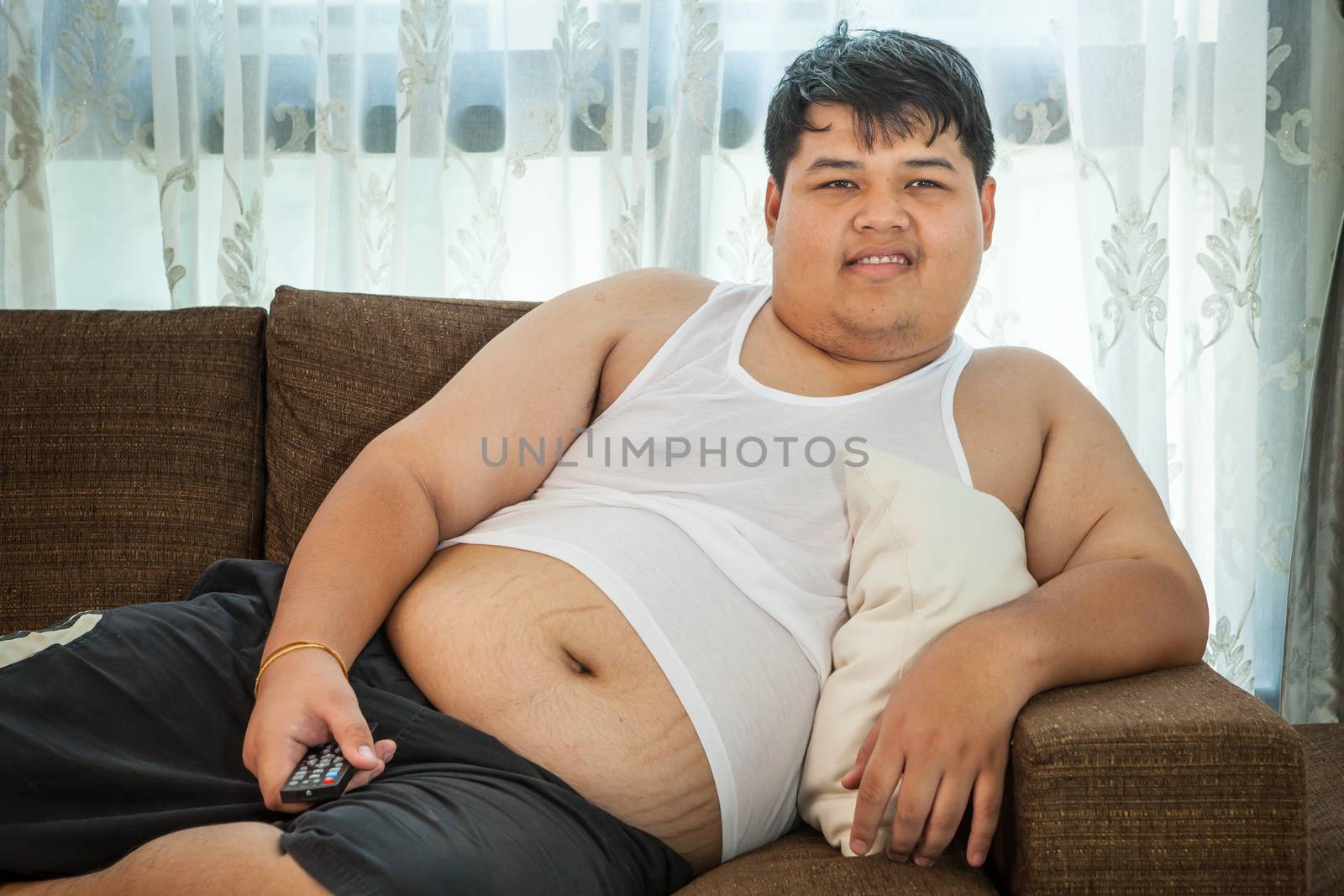 Overweight asian guy sitting on the couch with remote in hand trying to watch some TV