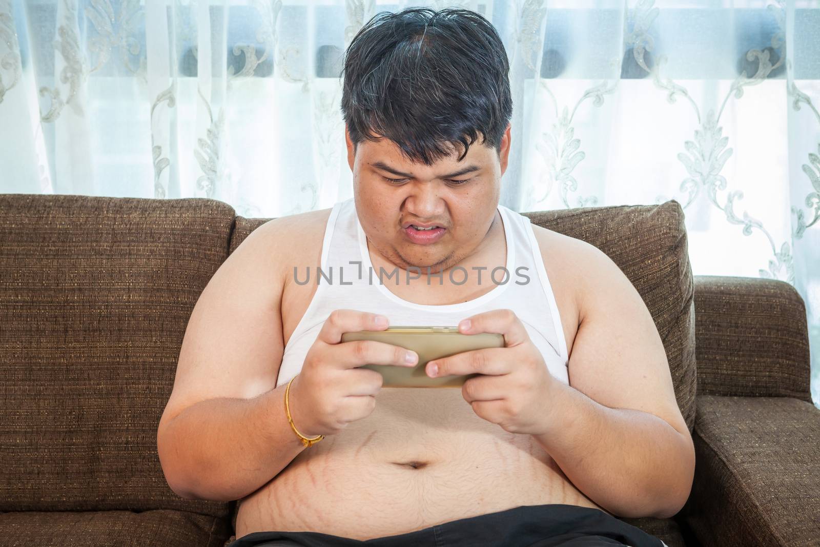 Fat asian man play game with his smartphone by witthaya