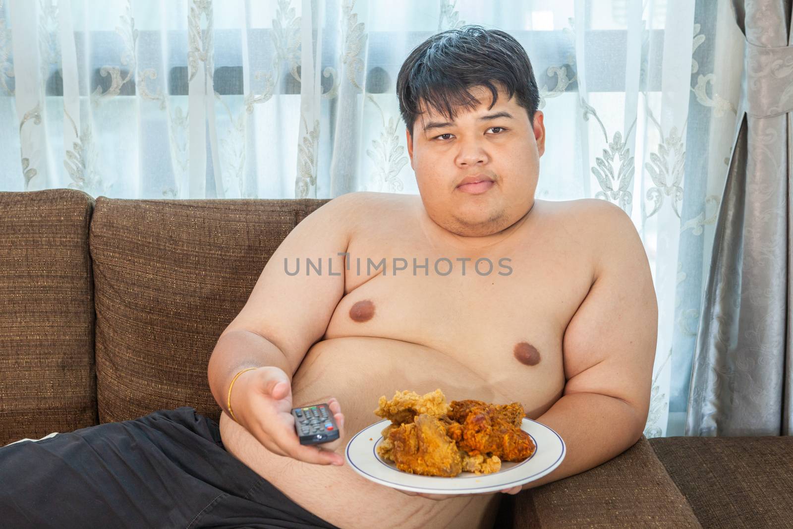 Lazy overweight asian male with fast food and watching television