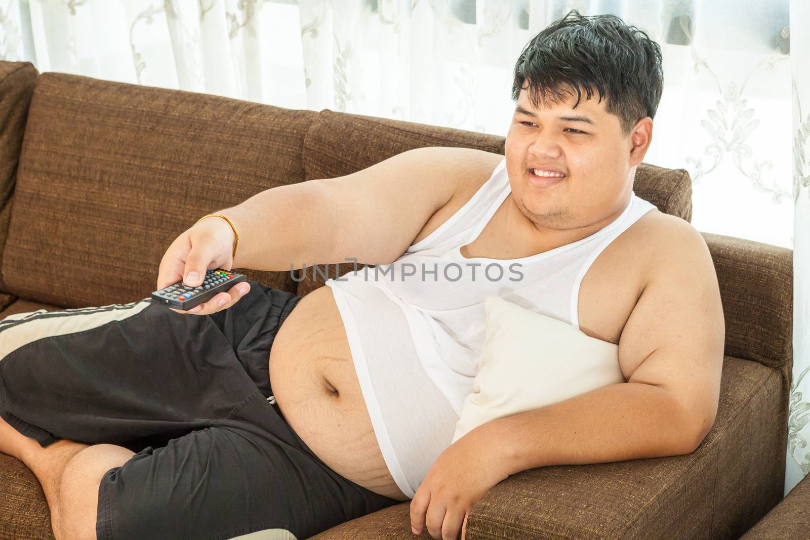 Overweight asian guy sitting on the couch with remote in hand trying to watch some TV