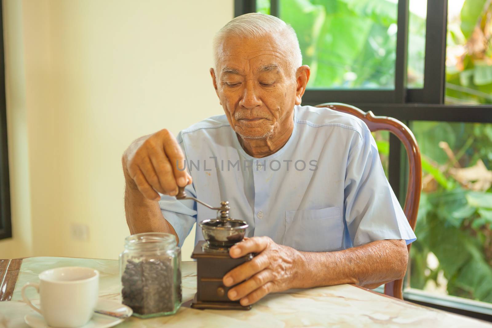 Asian senior man with vintage coffee grinder by witthaya