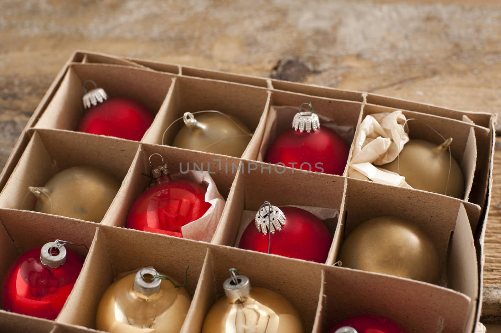 Open cardboard carton of rustic golden and red colored christmas tree ornaments balls on table