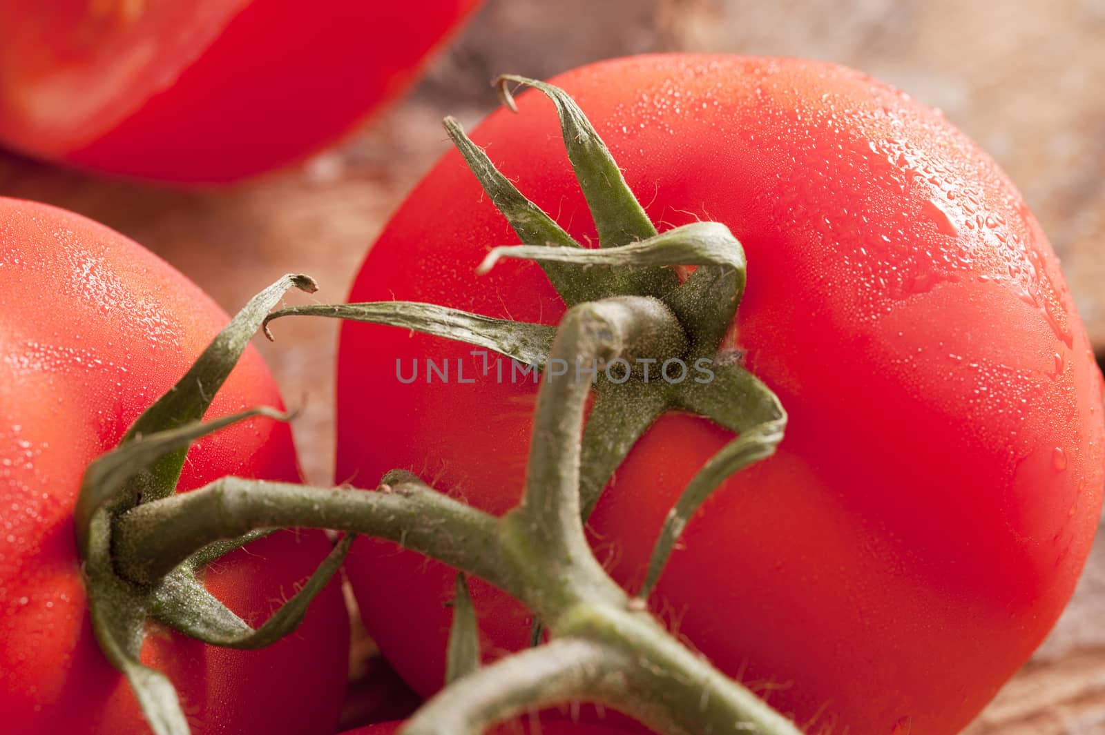 Detail close up on very ripe red tomatoes with green stems and moisture on the skin