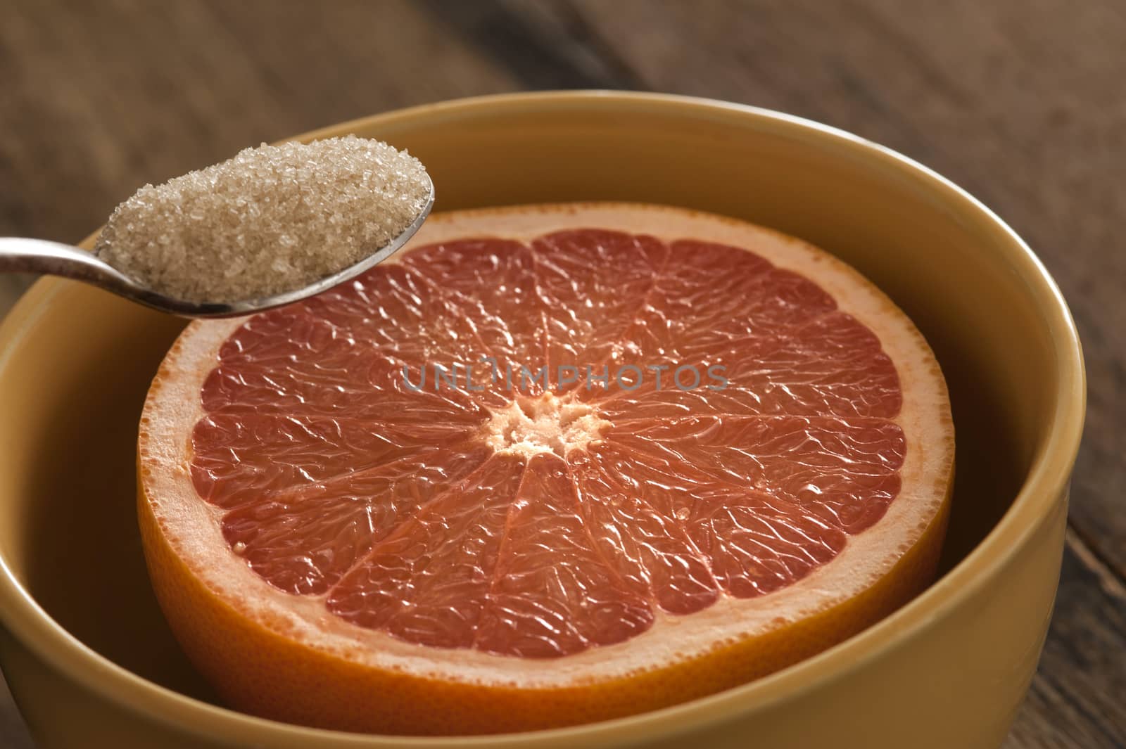 Close up of spoon with full of brown sugar being held above a freshly cut grapefruit half in bowl