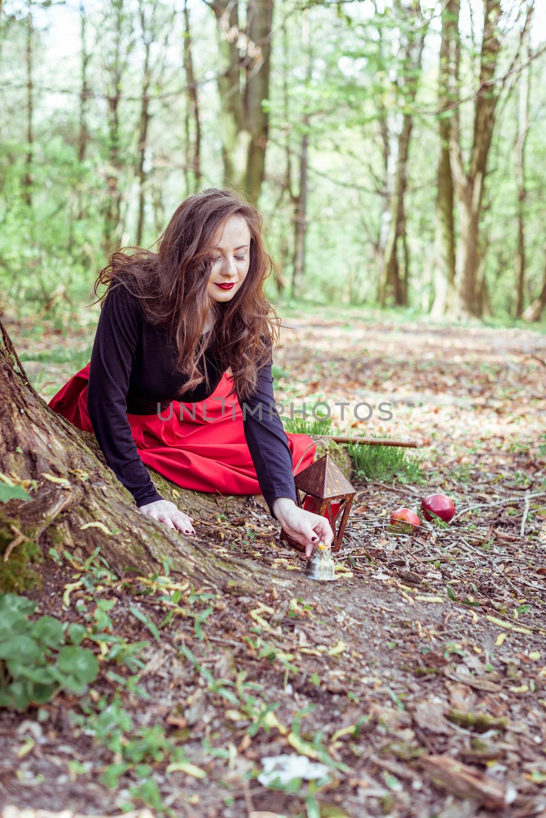 mystical witch woman in red dress lights a candle in the spring forest