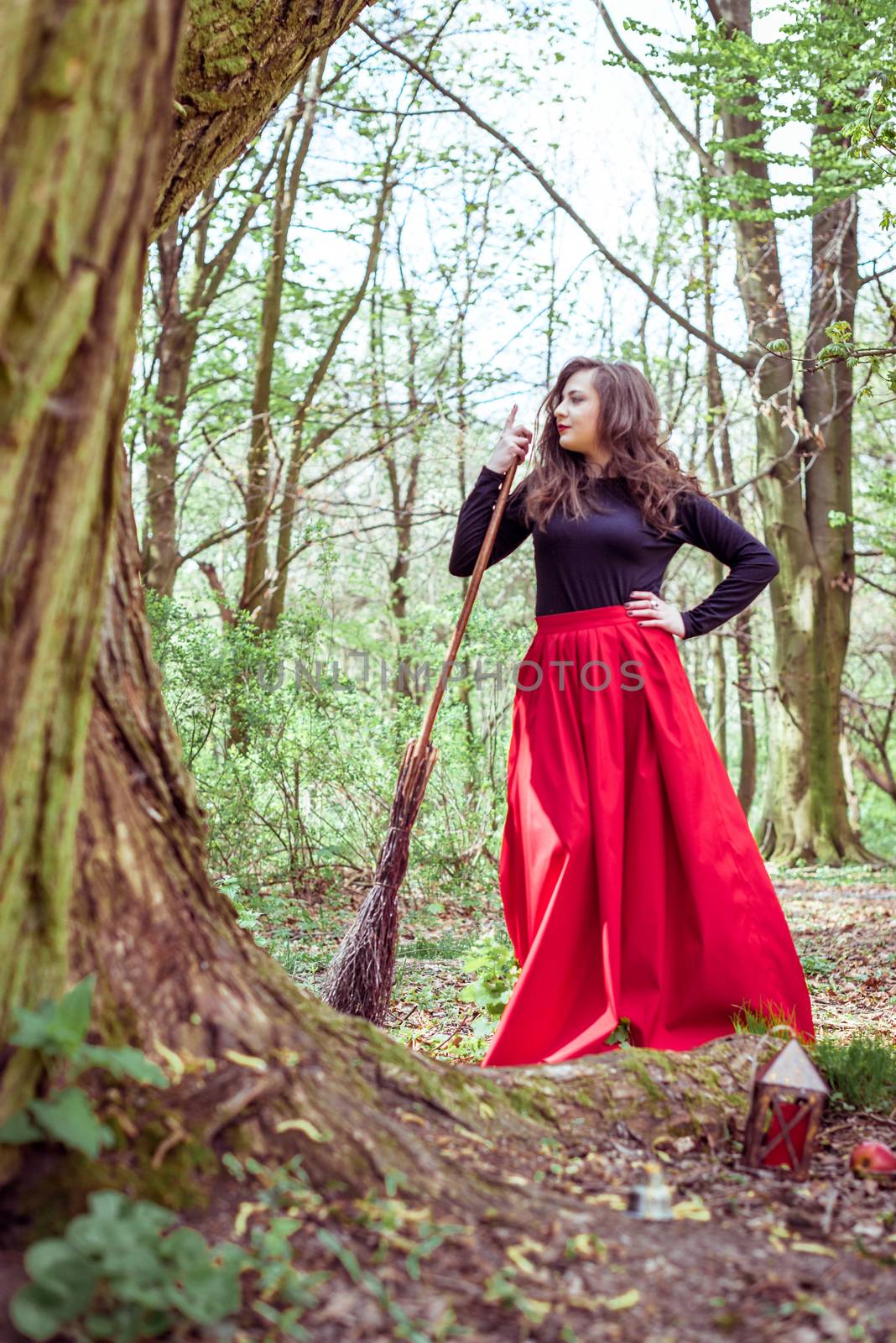 female witch standing with wooden broom in the spring forest