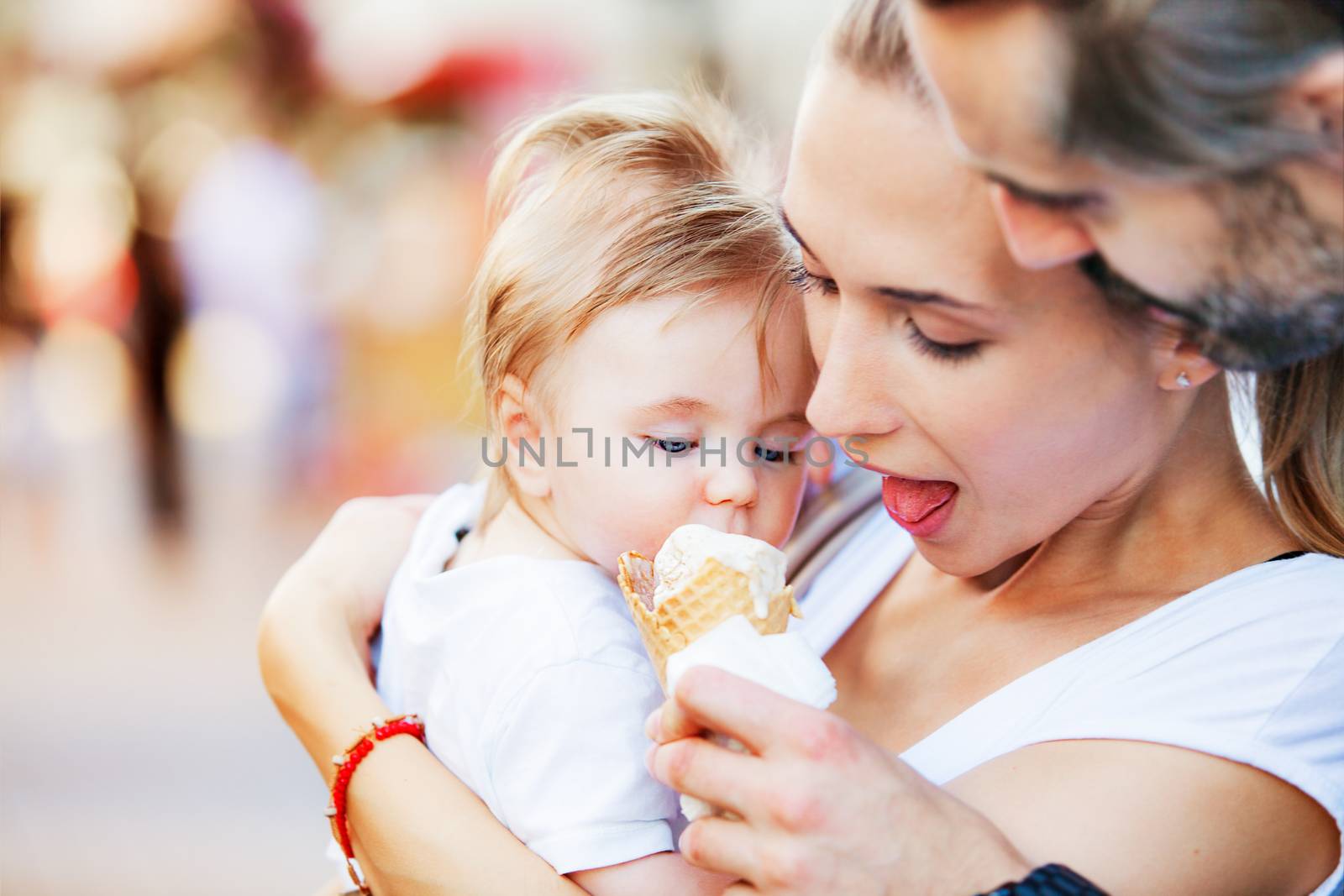 A baby boy is being hugged by his mother and father while fed with ice cream.