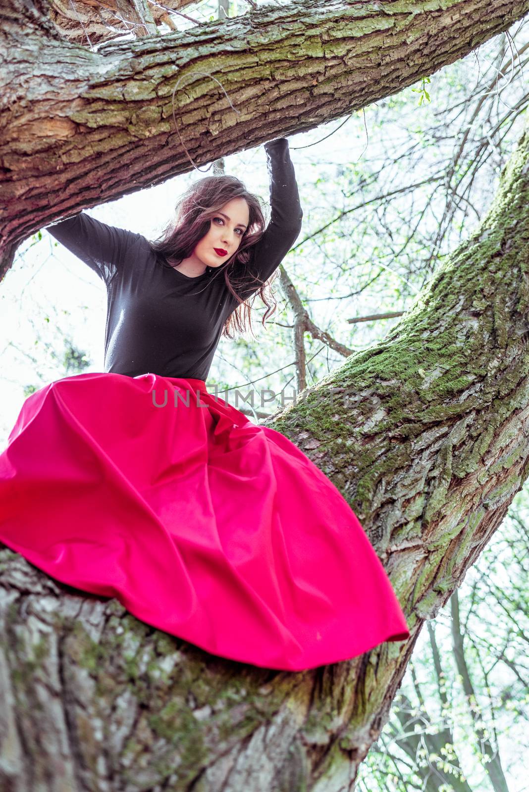 beautiful young woman in a red skirt sitting on a tree trunk in spring forest